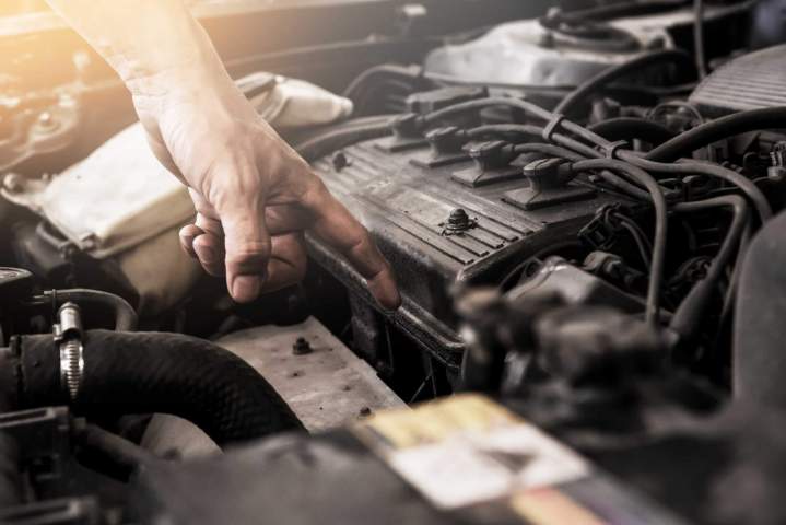 Un mécanicien professionnel en tenue de travail inspectant minutieusement le moteur dune voiture dans un garage moderne et bien éclairé, symbolisant lexpertise technique.
